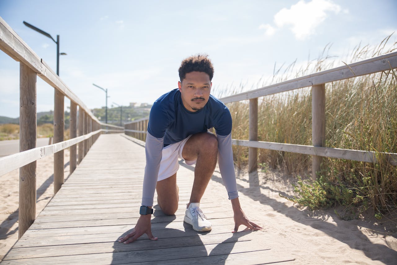 Man kneeling on a boardwalk in Portugal, ready to jog under a clear blue sky.